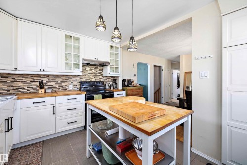 Kitchen featuring white cabinetry with dark hardware, wood-finish countertops, and a mosaic tile backsplash - 11607 141 Street, Edmonton, AB - Indoor Photo Showing Kitchen