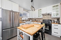 Kitchen featuring white cabinetry, butcher block countertops, stainless steel French door refrigerator, black range, and tile backsplash - 