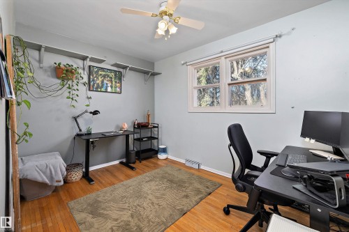 Hardwood flooring enhances this versatile room, featuring a white ceiling fan with integrated lighting, a single window, and light gray wall shelves - 11607 141 Street, Edmonton, AB - Indoor Photo Showing Office