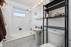 Full bathroom featuring a pedestal sink, white tiled walls, and a window with textured glass - 