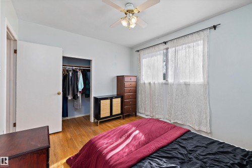 Hardwood flooring throughout, featuring a ceiling fan with integrated lighting, a spacious window with a black curtain rod, and a closet with a bi-fold door - 11607 141 Street, Edmonton, AB - Indoor Photo Showing Bedroom