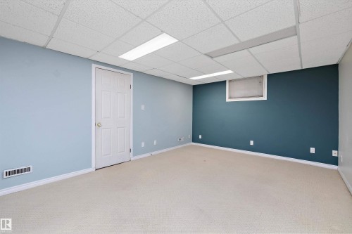 Carpeted interior space featuring a drop ceiling with integrated lighting, a painted accent wall, a white paneled door, and white baseboards - 11607 141 Street, Edmonton, AB - Indoor