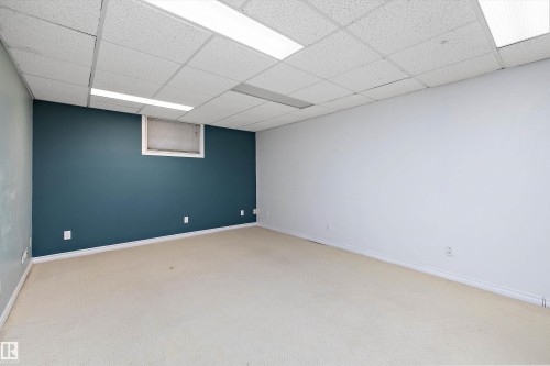 Carpeted room featuring a drop ceiling with integrated fluorescent lighting, a deep teal accent wall, and a white wall - 11607 141 Street, Edmonton, AB - Indoor Photo Showing Other Room