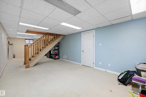 Finished basement area featuring a wood staircase with a carpeted runner, drop ceiling with recessed lighting, and light blue wall paint - 11607 141 Street, Edmonton, AB - Indoor