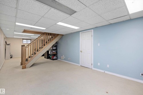 Carpeted lower level featuring a light wood staircase with balusters, a suspended acoustic ceiling with integrated lighting, a paneled door, and a small window - 11607 141 Street, Edmonton, AB - Indoor