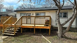 Rear exterior featuring a spacious wooden deck with railings and stairs, white siding, and a dark shingle roof - 