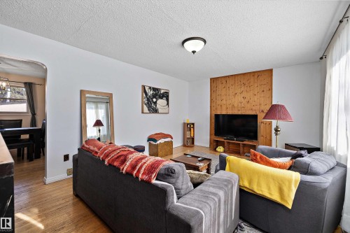 Living area featuring wood-finish flooring, a wood-paneled accent wall, a built-in media console, and a contemporary ceiling light fixture - 11607 141 Street, Edmonton, AB - Indoor Photo Showing Living Room