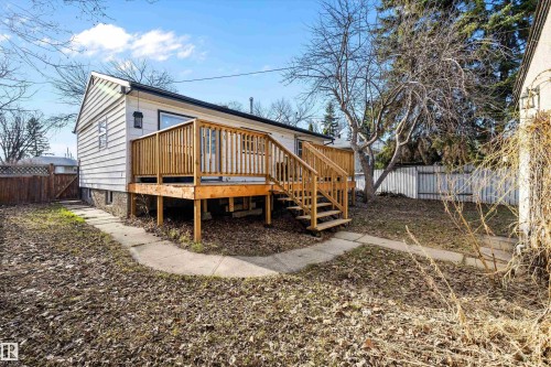 Rear exterior featuring a wood deck with railings and stairs, white horizontal siding, a fenced yard, and concrete pathways - 11607 141 Street, Edmonton, AB - Outdoor With Deck Patio Veranda