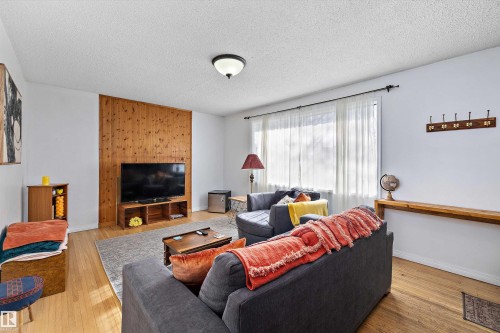 Living space featuring wood-finish flooring, a paneled accent wall, and a large window with sheer drapery - 11607 141 Street, Edmonton, AB - Indoor Photo Showing Living Room