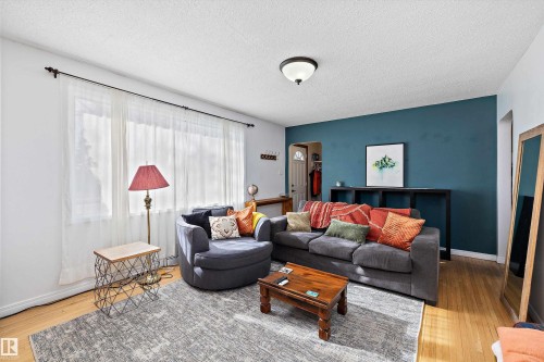 Living area featuring wood-finish flooring, a contemporary ceiling light fixture, a prominent accent wall, and a large window with sheer white curtains - 11607 141 Street, Edmonton, AB - Indoor Photo Showing Living Room