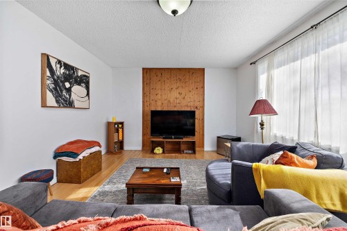 Living area featuring wood-finish flooring, a full-wall window with sheer drapery, and a wood-paneled accent wall - 11607 141 Street, Edmonton, AB - Indoor Photo Showing Living Room