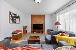 Living area featuring wood-finish flooring, a full-wall window with sheer drapery, and a wood-paneled accent wall - 