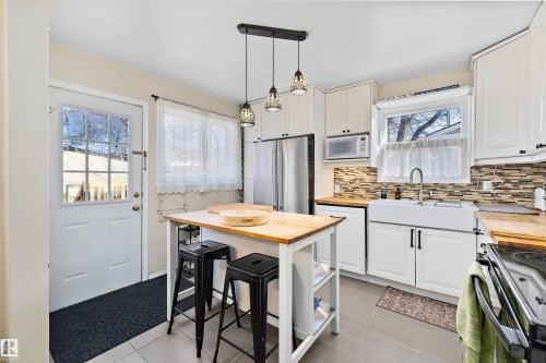 Well-appointed kitchen featuring white cabinetry, stainless steel appliances, butcher block countertops, a tile backsplash, and a farmhouse sink - 11607 141 Street, Edmonton, AB - Indoor Photo Showing Kitchen