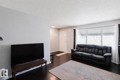 Spacious living area featuring dark wood-finish flooring, light grey walls, and a large window with white blinds - 10325 152 Street, Edmonton, AB - Indoor Photo Showing Living Room