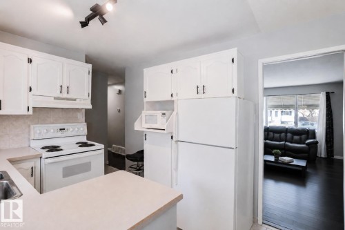 Kitchen featuring white cabinetry with black hardware, an integrated white electric range, and a dual-basin stainless steel sink - 10325 152 Street, Edmonton, AB - Indoor Photo Showing Kitchen