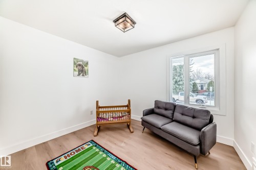 Bright room featuring a large window, neutral white walls, and wood-finish flooring - 8712 89 Avenue, Edmonton, AB 