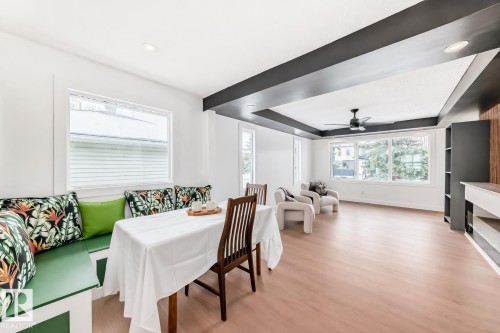 Open-concept living space featuring light wood-finish flooring, white walls, and a recessed ceiling with dark beams - 8712 89 Avenue, Edmonton, AB 