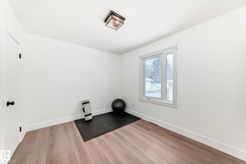 Bright room with wood-finish flooring, white walls, and a large window - 8712 89 Avenue, Edmonton, AB 
