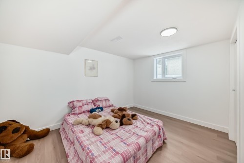 Bedroom featuring light wood-finish flooring, white baseboards, and a white ceiling with a flush-mount circular light fixture - 8712 89 Avenue, Edmonton, AB 