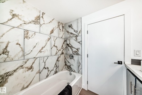 Bathroom featuring a white bathtub, large format marble-look wall tiles, and a white door with matte black hardware - 8712 89 Avenue, Edmonton, AB 