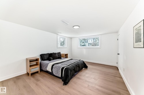 Room featuring wood-finish flooring, two windows, a white door with black hardware, white walls, and a flush-mount ceiling light - 8712 89 Avenue, Edmonton, AB 