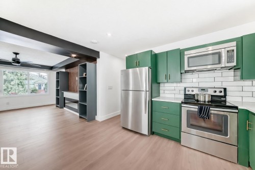 Modern kitchen featuring green cabinetry, stainless steel appliances, and white subway tile backsplash - 8712 89 Avenue, Edmonton, AB 