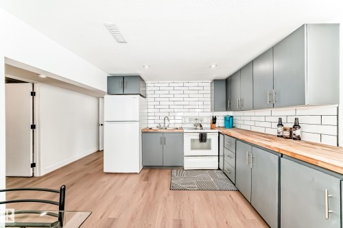 Kitchen featuring light wood-finish flooring, white subway tile backsplash, and light gray cabinetry with brushed nickel hardware - 8712 89 Avenue, Edmonton, AB 