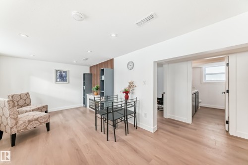 Spacious room featuring wood-finish flooring, recessed lighting, and a partial accent wall with vertical wood paneling - 8712 89 Avenue, Edmonton, AB 