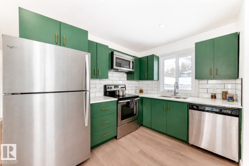 Kitchen featuring vibrant green cabinetry with brass hardware, stainless steel appliances, white subway tile backsplash, and light wood-finish flooring - 8712 89 Avenue, Edmonton, AB 