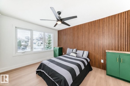 Room featuring a wood-slat accent wall, wide plank wood-finish flooring, and a contemporary ceiling fan with integrated lighting - 8712 89 Avenue, Edmonton, AB 