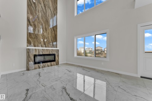 Spacious room featuring a floor-to-ceiling fireplace with a polished, veined surround, an integrated electric fireplace, and a white mantel - 12603 44 Street, Edmonton, AB - Indoor Photo Showing Other Room With Fireplace