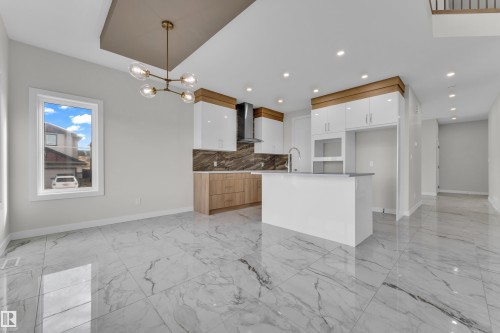 Open-concept kitchen and dining area featuring large format white and gray veined floor tiles, a kitchen island with seating, two-tone cabinetry with white high-gloss uppers and wood-finish lowers, a dark backsplash, and a modern chandelier - 12603 44 Street, Edmonton, AB - Indoor Photo Showing Kitchen