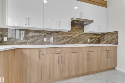 Contemporary kitchen with light wood-finish base cabinetry, white upper cabinetry, and a stone-look backsplash - 12603 44 Street, Edmonton, AB - Indoor Photo Showing Kitchen