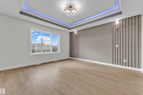 Spacious interior featuring wood-finish flooring, a tray ceiling with integrated lighting, and a modern light fixture - 12603 44 Street, Edmonton, AB - Indoor Photo Showing Other Room