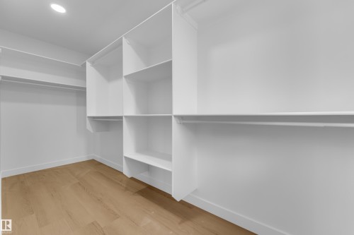 Walk-in closet featuring light wood-finish flooring, recessed ceiling lighting, built-in shelving, and multiple hanging rods - 12603 44 Street, Edmonton, AB - Indoor With Storage
