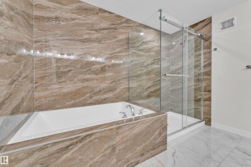 Bathroom featuring full-height marble-look wall tiling, a white built-in bathtub with deck-mounted fixtures, and a glass-enclosed shower with a sliding door - 12603 44 Street, Edmonton, AB - Indoor Photo Showing Bathroom