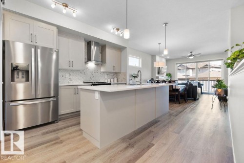Open-concept kitchen featuring an island with a light-toned countertop, stainless steel appliances, light wood-finish flooring, and a patterned tile backsplash - 3623 6 Street, Edmonton, AB - Indoor Photo Showing Kitchen With Upgraded Kitchen