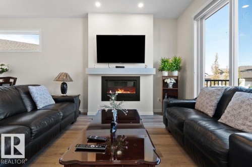 Living area featuring a floor-to-ceiling fireplace with a light-toned mantel, wood-finish flooring, recessed ceiling lighting, a large sliding glass door, and a horizontal transom window - 3623 6 Street, Edmonton, AB - Indoor Photo Showing Living Room With Fireplace