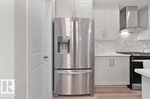 Stainless steel French door refrigerator set against light grey cabinetry, featuring a hexagonal tile backsplash, white countertops, and wood-finish flooring - 3623 6 Street, Edmonton, AB - Indoor Photo Showing Kitchen With Upgraded Kitchen