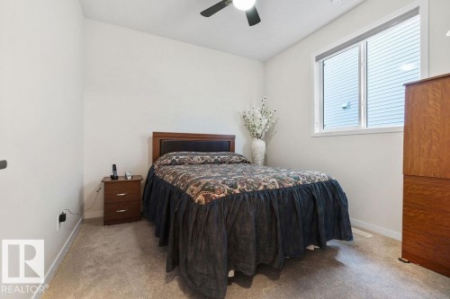 Carpeted room featuring a ceiling fan, a window with white trim, a wood-finish headboard, and light-toned walls - 3623 6 Street, Edmonton, AB - Indoor Photo Showing Bedroom