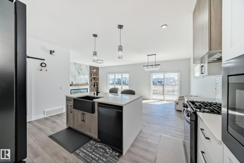 Modern kitchen island featuring a farmhouse sink, integrated dishwasher, and pendant lighting - 3247 Chernowski Way, Edmonton, AB - Indoor Photo Showing Kitchen With Stainless Steel Kitchen With Upgraded Kitchen