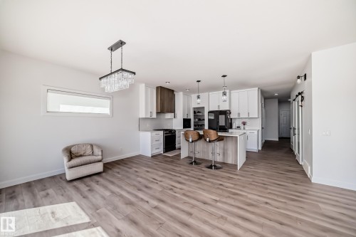 Open-concept living area featuring wood-finish flooring, a contemporary kitchen, and a crystal chandelier - 3247 Chernowski Way, Edmonton, AB - Indoor