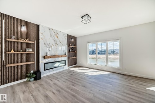 Living area featuring a modern linear fireplace with a stone surround, integrated wood shelving, and wood-finish flooring - 3247 Chernowski Way, Edmonton, AB - Indoor