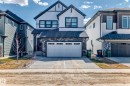 Modern two-story residence featuring a two-car garage, dark trim accents, stone facade detailing, white siding, and a prominent front entry with a dark door - 3247 Chernowski Way, Edmonton, AB  - Outdoor With Facade 