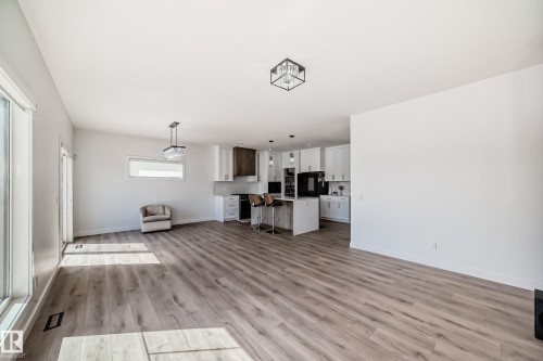 Spacious open-concept living area featuring wood-finish flooring, large windows, and a contemporary kitchen - 3247 Chernowski Way, Edmonton, AB - Indoor