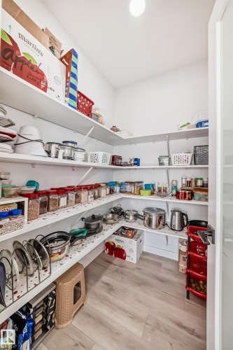 Spacious walk-in pantry featuring light wood-finish flooring and extensive white shelving - 3247 Chernowski Way, Edmonton, AB - Indoor With Storage