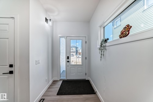 Entryway featuring a white paneled door with black hardware, wood-finish flooring, and a sidelight window - 3247 Chernowski Way, Edmonton, AB - Indoor Photo Showing Other Room