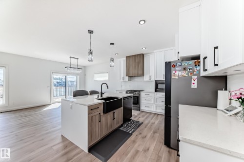 Modern kitchen featuring a central island with a farmhouse sink and pendant lighting, white cabinetry, integrated stainless steel appliances, and wood-finish flooring - 3247 Chernowski Way, Edmonton, AB - Indoor Photo Showing Kitchen