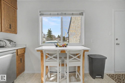 Kitchen area with a window providing outdoor visibility, light wood-finish cabinetry, white countertops, and patterned floor tiling - 17305 60 Ave, Edmonton, AB 