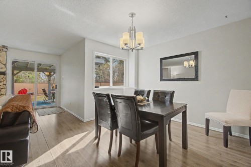 Living and dining area featuring wood-finish flooring, a contemporary chandelier, and a large window - 17305 60 Ave, Edmonton, AB 